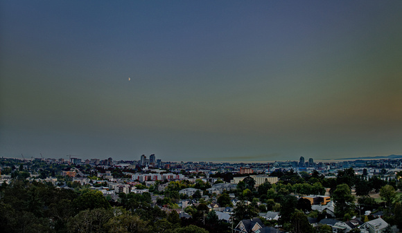 Blue hour with a smoky sunset highlighting a Quarter Moon over the city